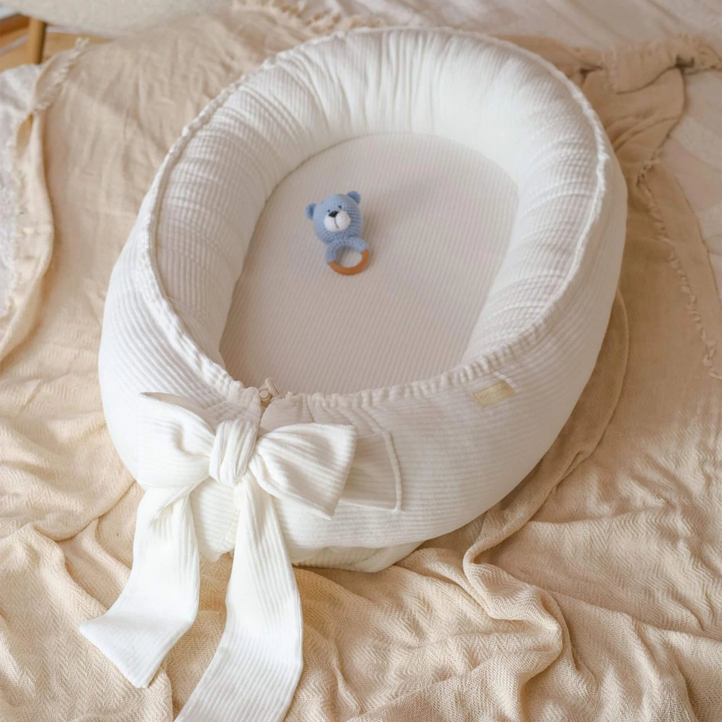 Baby Nestchen aus Cord in Creme in Gesamtansicht auf einem Bett